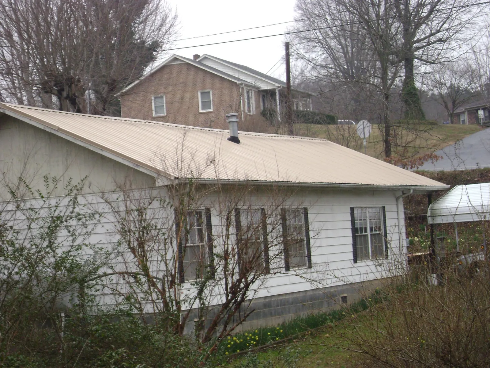 Tan metal roof on a white sided house set into a hillside — Commercial Roofing by Roofing Brothers in Stratford